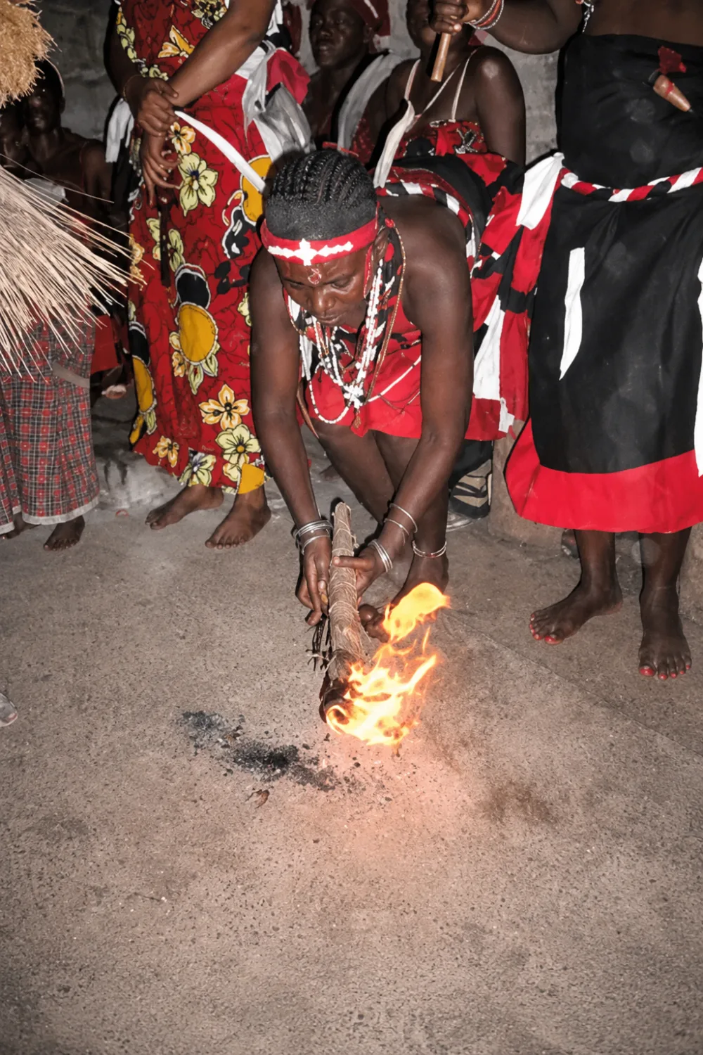 Un initié allume le feu rituel au cœur de la cérémonie de nuit, la communauté autour