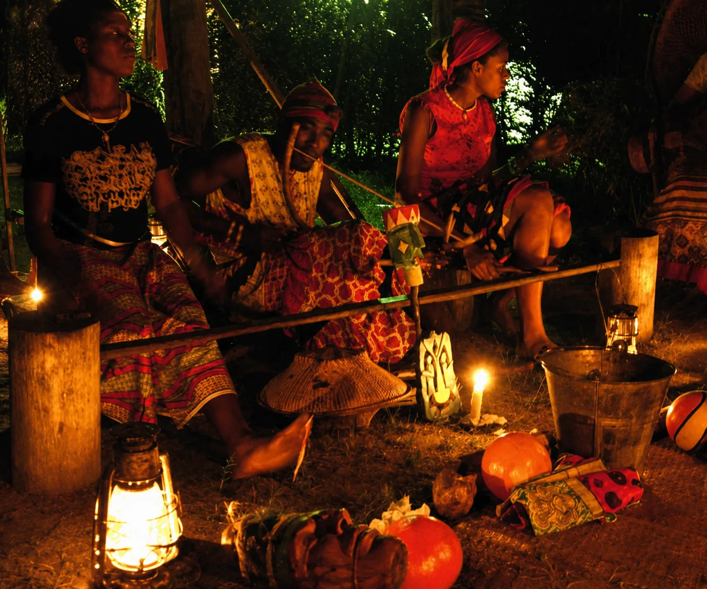 Cérémonie d'initiation au Bwiti à la nuit tombée, femmes en tenues traditionnelles assises autour de bougies et d'objets rituels à Ebando